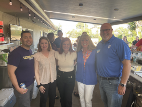 three women and two men standing together in front of an outdoor kitchen at a social gathering